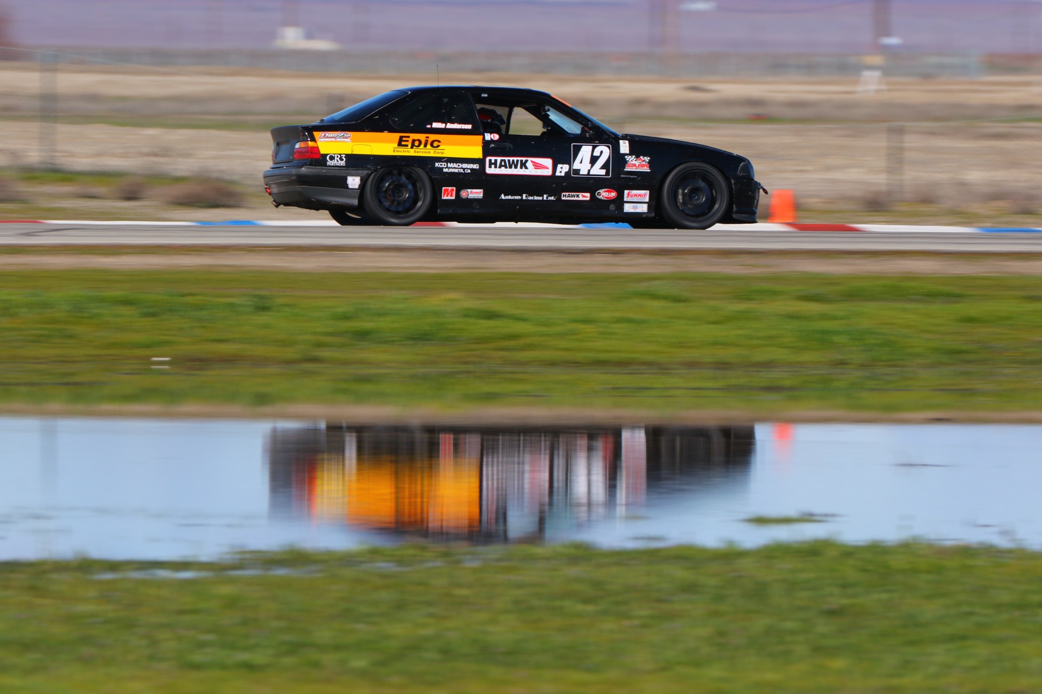 Side view of Mike Anderson's black and orange number 42 E36 BMW at speed