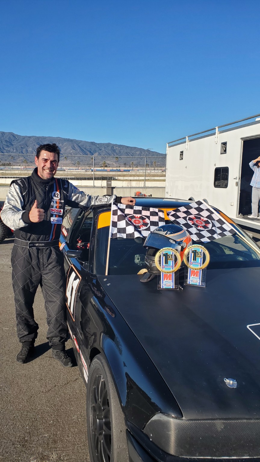 Mike Anderson beside the E36 BMW with checkered flags and race awards
