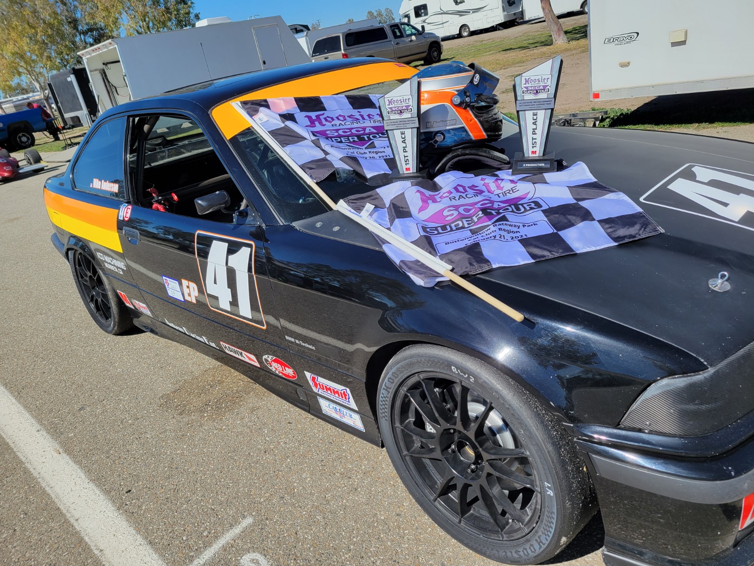 E36 BMW race car displayed in the paddock with awards and memorabilia