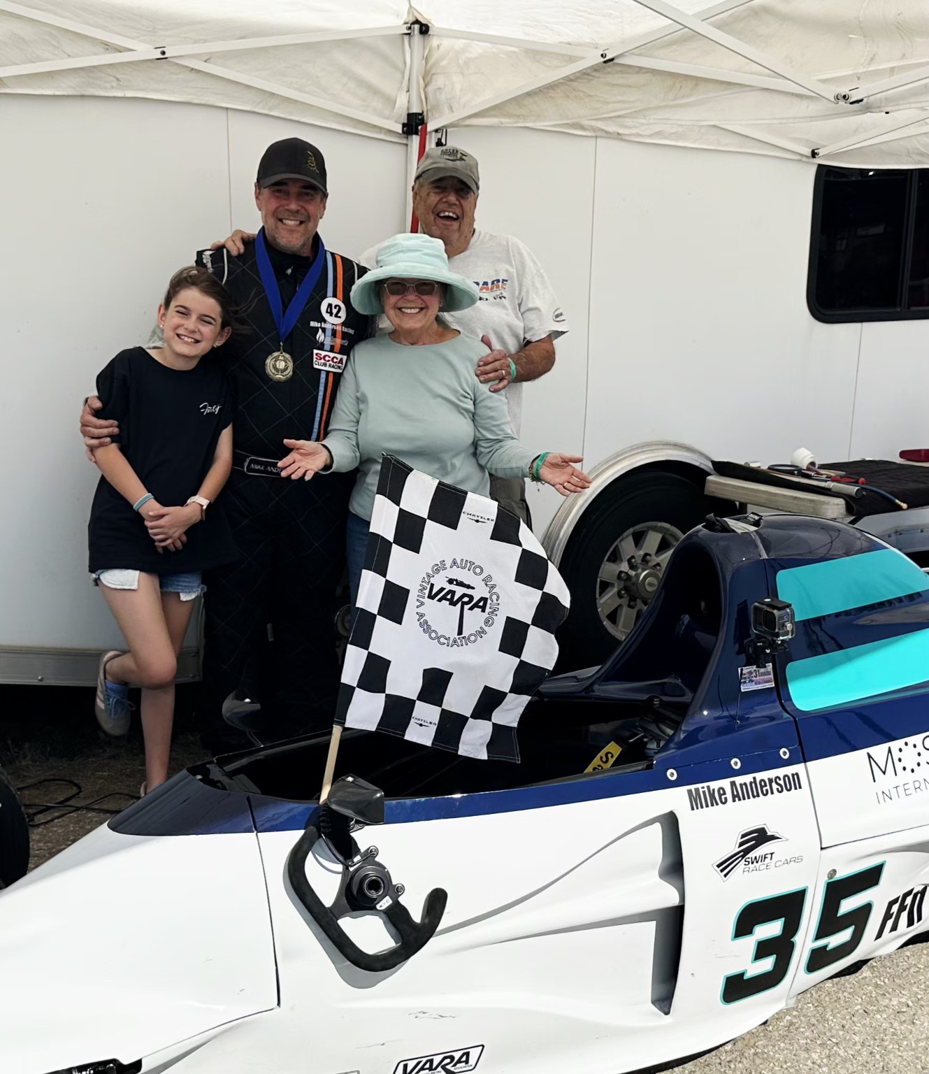 Mike Anderson celebrating a Buttonwillow victory with family, a medal, checkered flag, and the restored Swift DB1 number 35